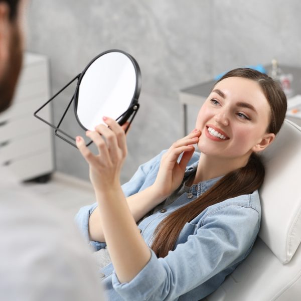 Young,Woman,Looking,At,Her,New,Dental,Implants,In,Mirror